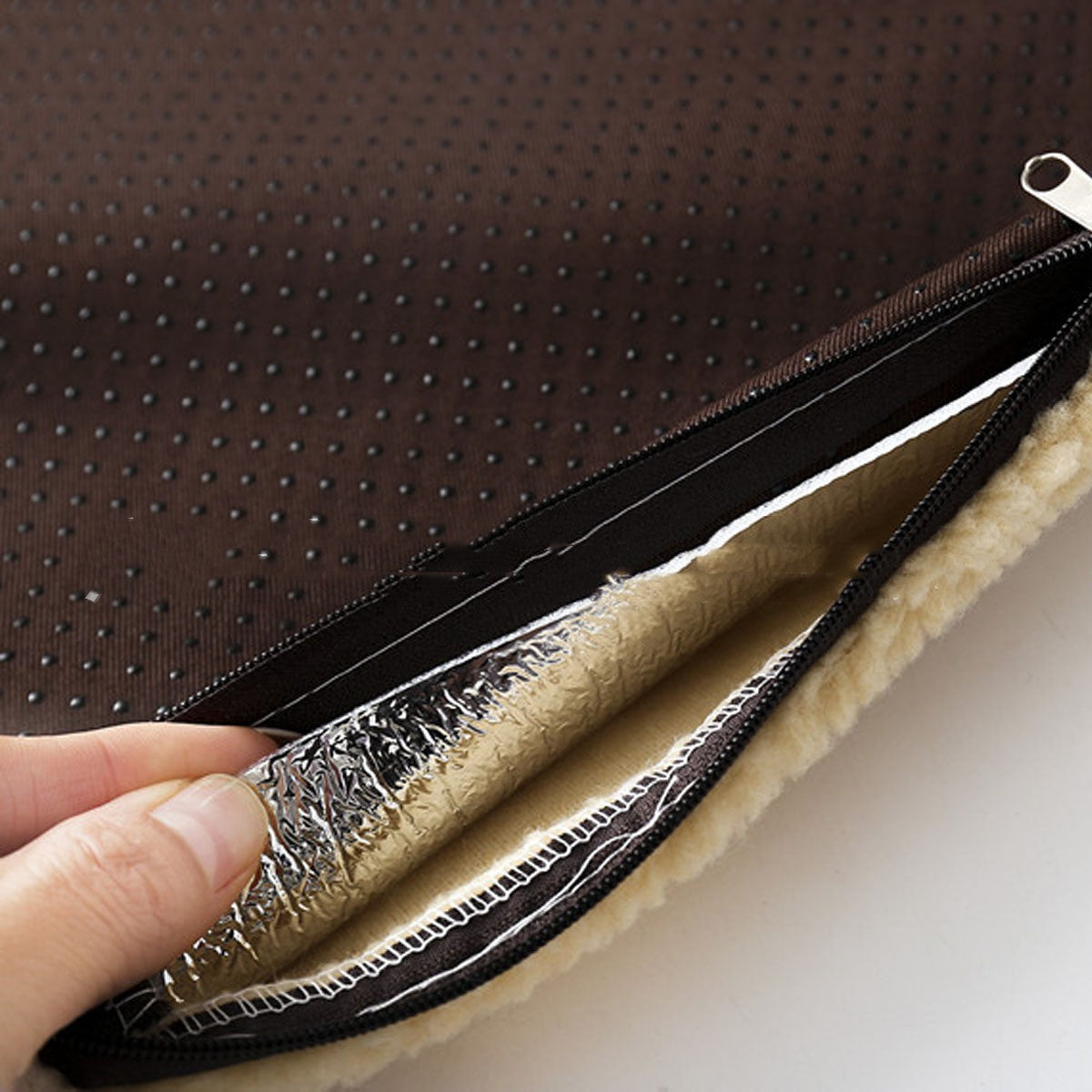 Close-up of a hand holding a metallic object against a textured brown background