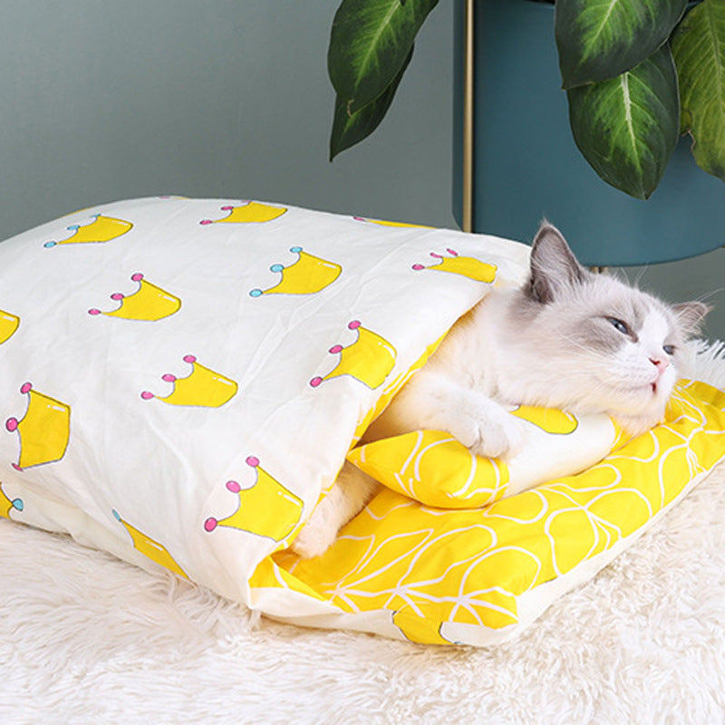 Cat peeking out from a yellow and white patterned blanket with crowns on a fluffy surface.