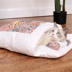 Cat lying inside a large white pet bed with colorful cat-themed pillow on a wooden floor.