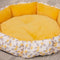 Round pet bed with yellow cushion and floral patterned border on a carpeted floor.