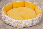 Round pet bed with yellow cushion and floral patterned border on a carpeted floor.