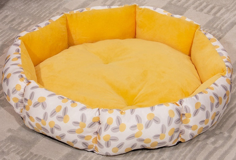 Round pet bed with yellow cushion and floral patterned border on a carpeted floor.