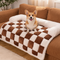 Corgi dog on a checkered pet bed in a cozy living room.