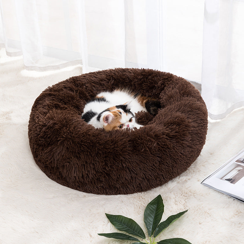 A pet bed in a round shape with a brown color, where a white cat is resting inside.